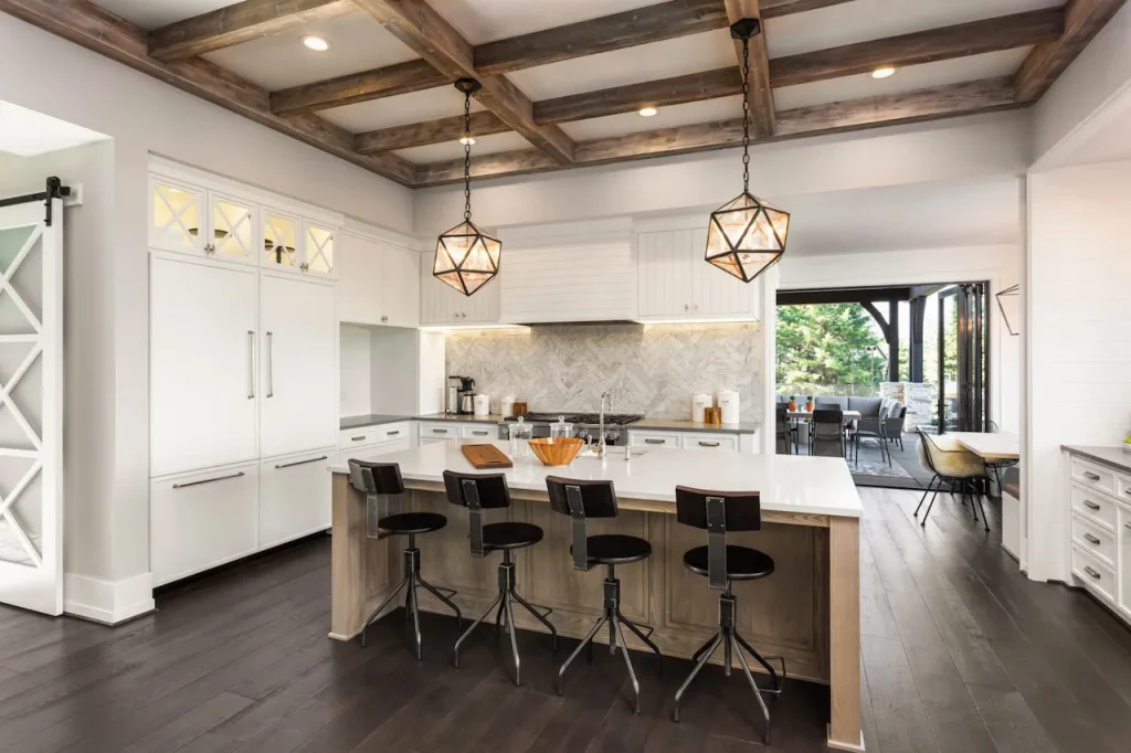 Modern farmhouse kitchen with white cabinets, large island seating, wood beam ceiling, pendant lighting, and open access to outdoor patio.