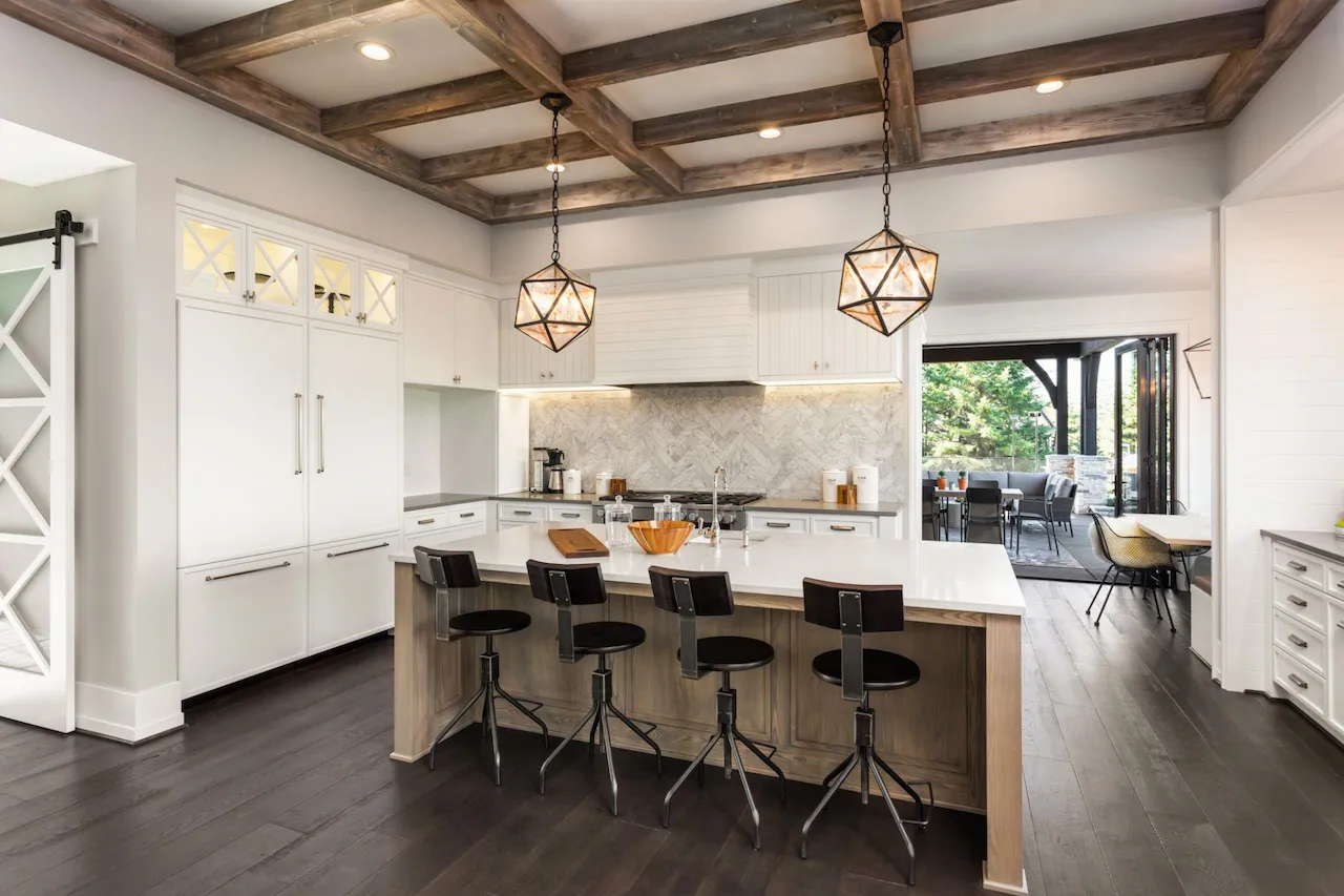 Modern farmhouse kitchen with white cabinets, large island seating, wood beam ceiling, pendant lighting, and open access to outdoor patio.